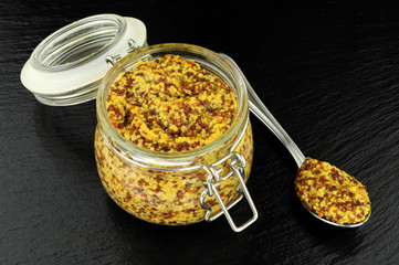 Glass storage jar filled with wholegrain mustard on a slate stone, background