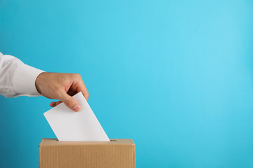 Man putting ballot into voting box on blue background