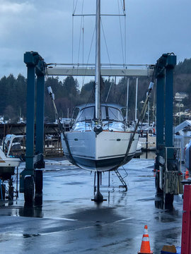 Sailboat on slings being lifted out of the water for maintenance at a boat yard