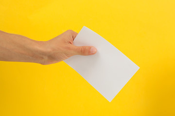 Male hand holding blank paper on yellow background