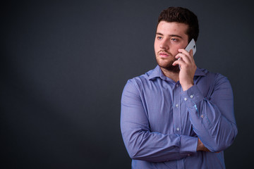 Portrait of young handsome overweight bearded businessman talking on the phone