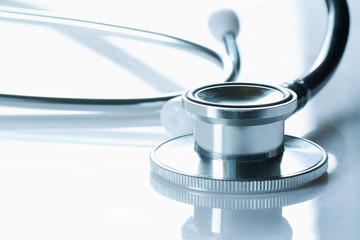 Stethoscope on glossy white table, the black phonendoscope, close up on white background,