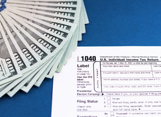 Tax form 1040 and dollars on a blue table. The concept of business taxation and business