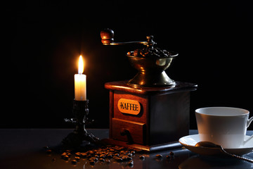 coffee grinder, a cup of coffee and coffee beans in the candlelight