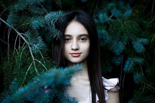 Black and white portrait of a beautiful teen girl posing between the pine branches.