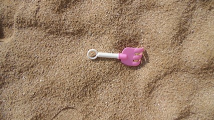 Children's plastic toy lying in the sand. Pink rake for sand. Family summer vacation.