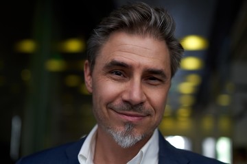 Naklejka premium Portrait of happy mature man smiling and looking at camera. Confident businessman wearing suit, standing in office building hallway.