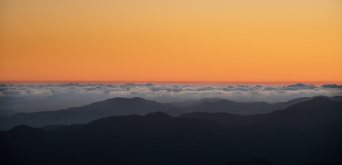 Colourful sunset with orange color above the clouds and the mountains.