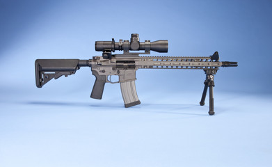 AR 15 style rifle with a magazine inserted, shot in studio on a light blue background.