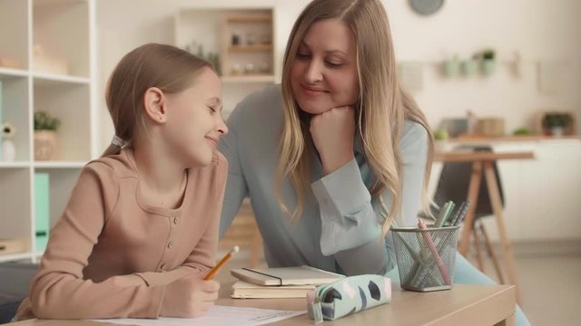 Medium shot of Caucasian blond-haired woman is checking on her daughter doing homework. Then woman is going cooking lunch