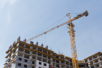 Fototapeta na wymiar Crane and building construction site against blue sky. Construction of a concrete apartment building. Modern construction