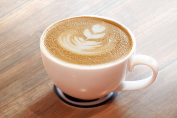 Cup of cappuccino with picture on milk foam on beige wooden background.