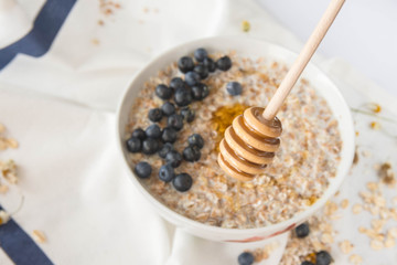 Healthy breakfast ingredients. A plate of porridge, a mug of milk and a mug of honey on a white background towel, view from above