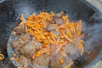 Cooking pilaf in a cauldron on the grill outside in the summer