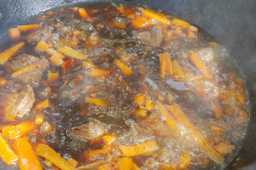 Cooking pilaf in a cauldron on the grill outside in the summer