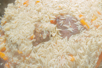Cooking pilaf in a cauldron on the grill outside in the summer