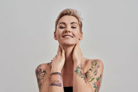 Beauty portrait of a young attractive half naked tattooed woman with perfect skin smiling at camera isolated over grey background