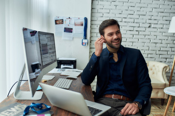 Good talk. Young successful businessman or sales manager wearing wireless earphones, talking with client or partner and smiling, working in the modern office