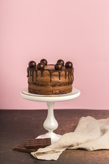 Chocolate birthday cake, white cake stand, chocolate bar, napkin,pink background.Vertical format.