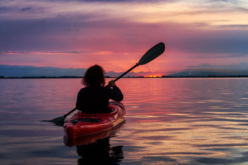 Sea Kayaking in calm waters during a colorful and vibrant sunset. Adventure Girl in Red Kayak....