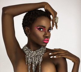 A portrait of a sexy young black female with short black hair, popping pink lip stick, perfectly manicured nails wearing a big diamond necklace in front of a bright background.