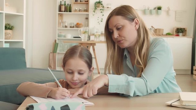 Medium shot portrait of beautiful Caucasian woman and her teenage daughter are sitting at desk in living room, doing math homework together and hugging