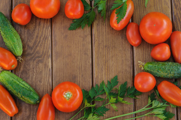 Frame from vegetables on a wooden background. Tomatoes, cucumbers, parsley. View from above.