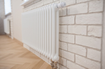 Fototapeta premium radiator and thermostat in the apartment - heater close-up. Apartment interior - radiator on a white brick wall.