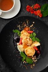 Ukrainian cheesecakes with sauces, berries and mint in a dark plate on a dark background

