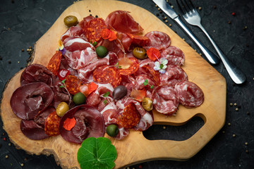Smoked meat, sausages, parma, jamon on a wooden board and a dark concrete table.