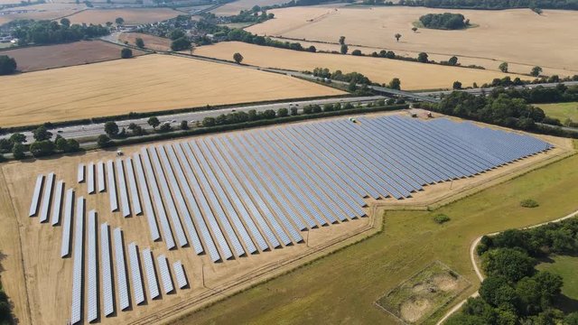Drone fly over Solar Farm, Aerial highview of a Solar Power Station with a nice landscape and busy highways and a small town on the background.
