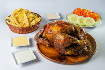 Delicious whole grilled chicken with french fries, salad and creams on wooden plate. Peruvian food "pollo a la brasa con papas fritas". White background.