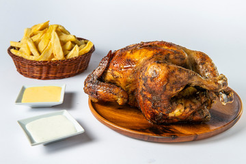 Peruvian food: "Pollo a la brasa con papas fritas" or grilled chicken with french fries and creams on wooden plate.  White background.