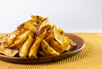 Potato wedges on wooden plate and white background. Front view.
