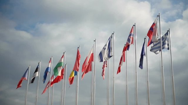 Many of national flags at windy day with cloudy sky at background.