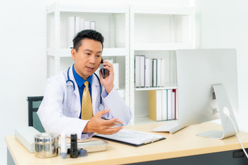 Asian man doctor writing document white talking to consulting patient by telephone or mobile phone. Telemedicine, telehealth concept. .