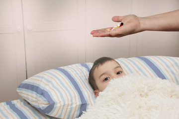 Obraz na płótnie Canvas female hand holds out, offering, a handful of colored pills and capsules, close-up, blurred image of a lying child in the background, copy space, concept of medical care, treatment