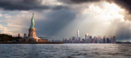 Panoramic view of the Statue of Liberty and Downtown Manhattan in the background during a vibrant cloudy sunrise. Taken in New York City, NY, United States. © edb3_16