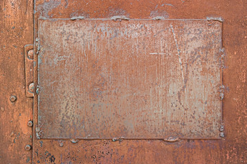 A rusty metal plate welded to an iron door with peeling brown paint, scratches and scuffs 