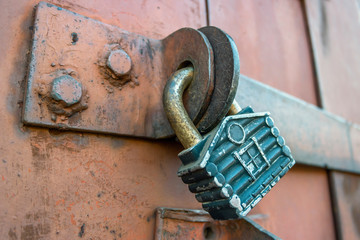 Locked metal padlock in the form of a house on the rusty iron gate