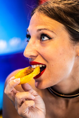 Extreme close up of the face of a sexy blonde woman with blue eyes eating a fried onion ring, retro color and florida background portrait image
