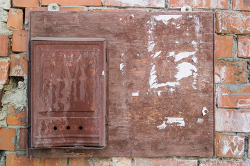 Old wooden Bulletin Board with scraps of torn paper and a bent and rusty metal mailbox hanging on a brick wall