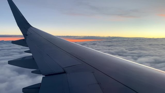 View out airplane window, plane wing above clouds at colorful sunset