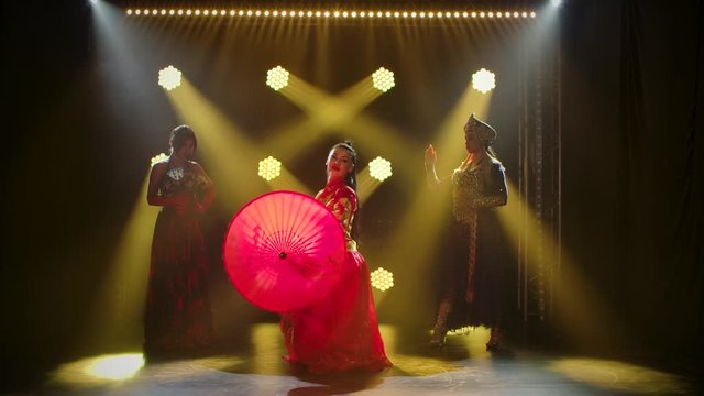 Girls dance in sexy theatrical costumes. Young hot brunettes with long hair. Bright makeup and red lips. Neon light effects and smoke. Modern sexy theatrical dance show. Slow motion.
