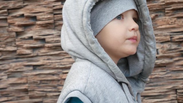A portrait of a cute little boy dressed in oversized vest with a hood