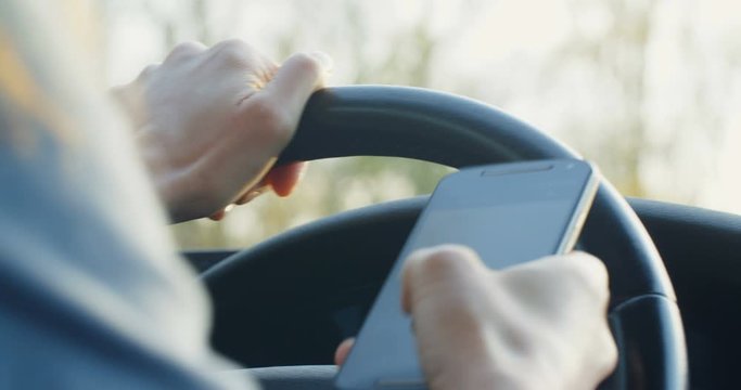 Close up shot of a woman using a smartphone while driving a car.