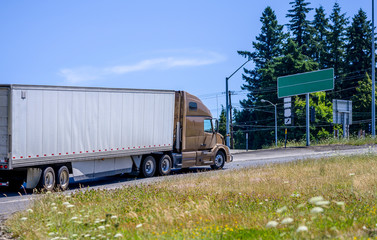 Brown big rig semi truck with dry van semi trailer climbing on the uphill road