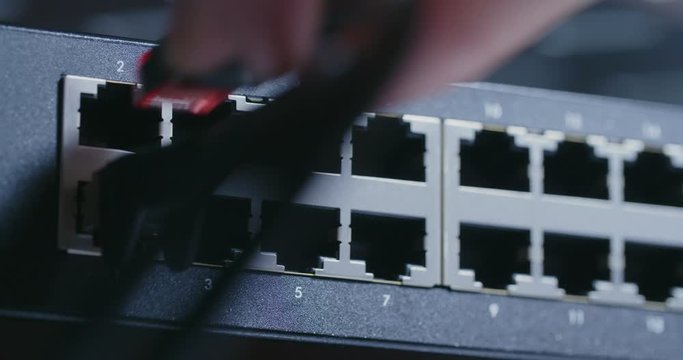 Hand plugs network patch cables into a switch. Closeup shot.
