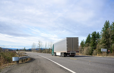 Fototapeta na wymiar Green big rig semi truck transporting frozen cargo in shine stainless steel refrigerator semi trailer running on the safety road