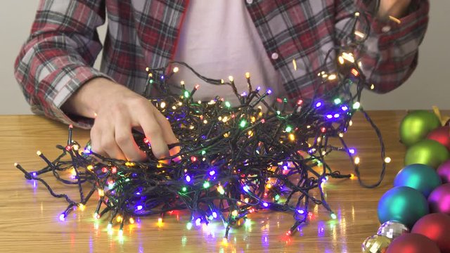 Decorative Christmas garland . Male hands trying to unravel the tangled glowing lights of garland at home